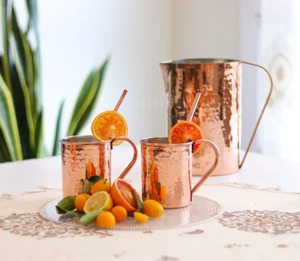 A close-up shot of a Cylindrical Copper Mug filled with a chilled Moscow Mule. A hand holding a Cylindrical Copper Mug against a backdrop of rustic wooden bar. A stack of Cylindrical Copper Mugs arranged on a kitchen counter. A close-up shot of the mug's hammered copper exterior, highlighting its intricate craftsmanship. A detail shot of the mug's tin-lined interior, emphasizing its food-safe construction.